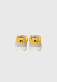 Nike SB tenisice s gornjim dijelom od sive suede kože i žute tkanine, s bijelim potplatima i crnim logotipom na peti. Glatka tekstura i zaobljen oblik.