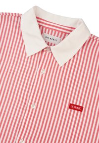 Czerwona i biała koszula w paski z białym kołnierzykiem, z małym czerwonym haftowanym logo na piersi oraz białymi guzikami.