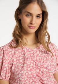 Blomstret bluse i pink med hvide blomster. Blødt stof, rund halsudskæring og korte puffærmer. Har samlede detaljer foran.