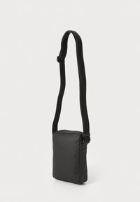 Černá nylonová crossbody taška obdélníkového tvaru, s nastavitelným popruhem, zipovým uzavřením nahoře a hladkým povrchem.