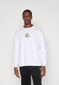 Λευκό βαμβακερό μπλουζάκι με μακριά μανίκια και πολύχρωμο σχέδιο βατράχου και μανιταριού στο κέντρο. Συνδυασμένο με μαύρο παντελόνι από κοτλέ.