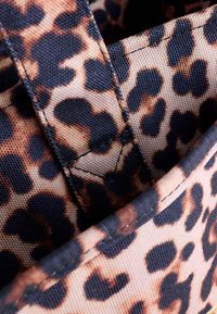 Geantă din material cu imprimeu de leopard, cu pete negre și maro proeminente, având o textură fină și bretele asortate. Interiorul prezintă cusături vizibile.