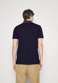 Navy blue polo shirt with white trim on the collar and sleeves. Short sleeves, side slits at the hem, made from a smooth fabric.