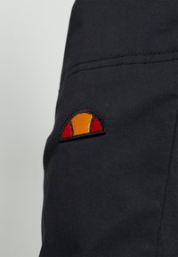 Gros plan sur un tissu noir avec un écusson de logo en demi-cercle cousu orange et rouge.