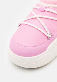 Baskets roses avec une tige en tissu texturé et des accents en caoutchouc lisse. Lacets blancs en croix sur la languette avec une semelle épaisse et rembourrée.