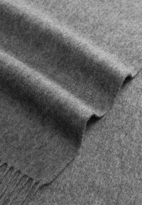 Weiches graues Wollgewebe mit einem gefalteten Rand und fransigem Besatz, der Textur und Dicke im Nahaufnahmen-Detail zeigt.