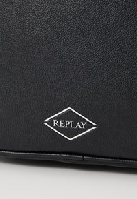 Borsa in pelle nera texturizzata caratterizzata da un logo a diamante argentato con il testo "REPLAY", che enfatizza un design elegante e resistente.