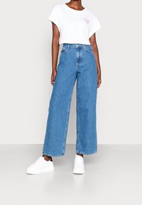 White short-sleeve t-shirt with a heart graphic, paired with wide-leg blue denim jeans and white sneakers. Smooth texture, casual design.