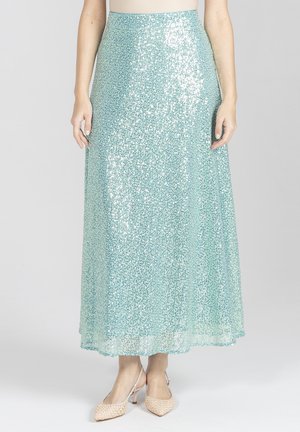 Kobieta w długiej, jasnoniebieskiej spódnicy z cekinami z subtelnym kwiatowym wzorem i beżowych szpilkach z ostrym noskiem.