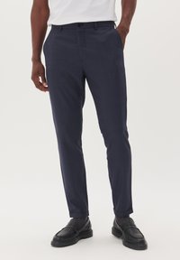 Pantaloni a quadri blu navy con una vestibilità su misura, frontale piatto e tasche laterali; abbinati a scarpe in pelle nere per un aspetto raffinato.