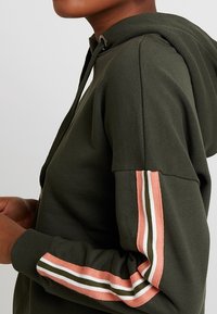 Donkergroene hoodie met een voorvak, verstelbare capuchon en duidelijk zichtbare gestreepte accenten in roze, wit en olijfgroen op de mouwen.