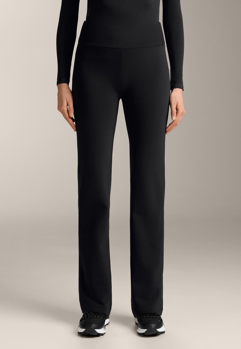 Čierne športové nohavice s širokým pásom, vyrobené z hladkej, elastickej tkaniny. Spárované s čiernymi teniskami s bielymi akcentmi.