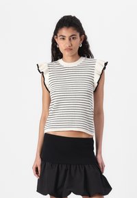 Strikket ermeløs topp med svart og hvit stripe, med volanger på ermene og en cropped design. Bæres med et svart volang skjørt.