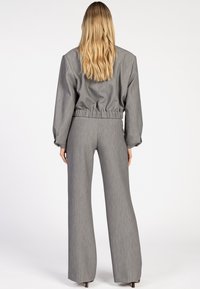 Grijze op maat gemaakte jas met elastische tailleband, gecombineerd met grijze wijde broek. Glad textuur, minimalistisch ontwerp en lange mouwen.