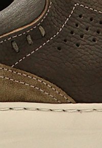 Zapatillas de cuero marrón oscuro con un acento de ante, detalle perforado, costuras blancas y una suela de goma beige.