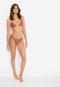 Σετ μπικίνι σε σκουριά χρώμα με τοπ τριγωνικό και μαγιό με δεσίματα στο πλάι, με υφή και μίνιμαλ σχεδιασμό.