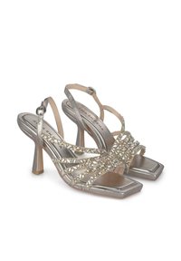Silberne High-Heelsandalen mit quadratischer Zehenpartie, ausgestattet mit überkreuzten Riemen, die mit klaren Edelsteinen verziert sind, sowie einem Knöchelriemen.