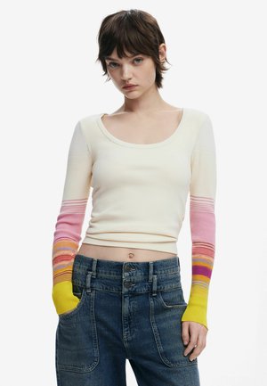 Cremfarbener Pullover mit langem Arm und gerippter Textur. Die Ärmel verlaufen von Pink zu Gelb und haben horizontale Streifen. Kombiniert mit hochtaillierter Jeans.