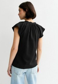Top negro de manga corta con detalle de espalda fruncida y una textura suave, combinado con jeans azul claro. Diseño simple y de corte relajado.