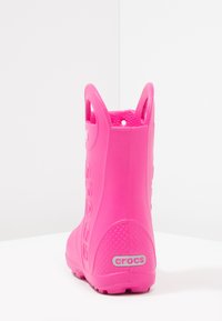 Botte de pluie en caoutchouc rose avec poignées latérales, semelle texturée et un logo "crocs" bien visible au niveau du talon. Matériau lisse et imperméable.