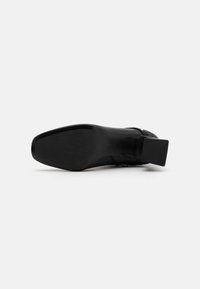 Black heeled shoe with a smooth leather upper, a square heel, and a textured rubber sole. Clean design with no visible embellishments.
