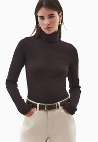 Brązowy prążkowany sweter z wysokim kołnierzem, z długimi rękawami. Połączony z jasnobeżowymi spodniami i ciemnobrązowym paskiem ze złotą klamrą. Gładka faktura.