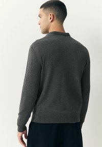 Suéter gris hecho de material de punto, con un cuello redondo, mangas largas y acentos de canalé en los puños y el dobladillo.