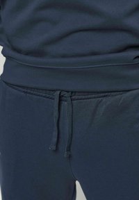 Mornarsko plave trenirka hlače s vezicom u struku i odgovarajuća mornarsko plava dukserica, prikazane na donjem dijelu tijela osobe.