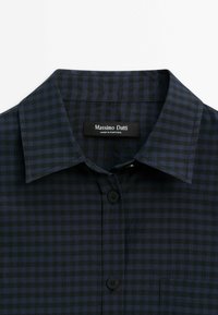 Chemise à carreaux bleu foncé et noir avec col, boutons noirs et une étiquette "Massimo Dutti Made in Portugal" à l’intérieur du col.
