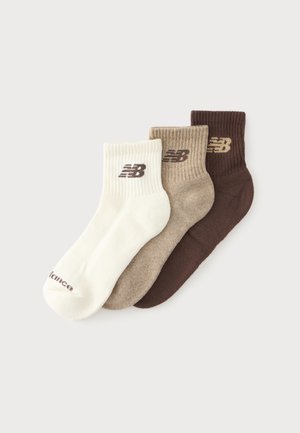Tre par ankelsokker i creme, lysebrun og mørkebrun, hver med et New Balance-logo nær skaftet, lagt fladt og delvist overlappende.