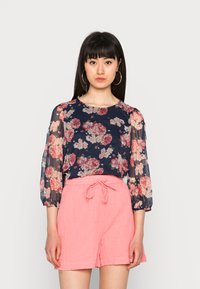 Blusa floral com fundo navy e mangas bufantes transparentes, combinada com calções de linho rosa com cintura elástica.