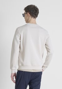 Lichtbeige sweatshirt met lange mouwen, een ronde halslijn en subtiele logodetail op de achterkant. Zacht, glad materiaal met geribbelde manchetten.