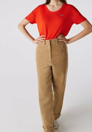 Rood katoenen T-shirt met korte mouwen en een ronde hals, gecombineerd met beige corduroy broek met hoge taille, verticale strepen en opgerolde pijpen.
