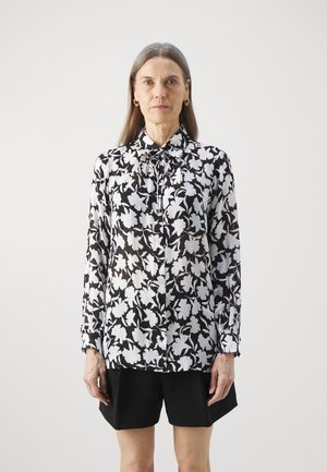 Langermet bluse i svart og hvitt blomstermotiv, med krage og knappelukking, kombinert med svarte shorts. Glatt, lett stoff.