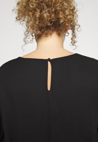 Blusa preta com decote redondo e detalhe em forma de buraco nas costas, preso por um pequeno botão preto. Tecido suave e liso com um design sem ornamentos.