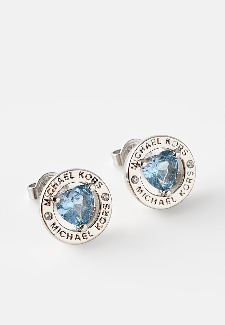 Okrągłe srebrne kolczyki z dużymi, sercowymi niebieskimi kryształami, udekorowane przezroczystymi kamieniami i wygrawerowanym napisem "MICHAEL KORS".
