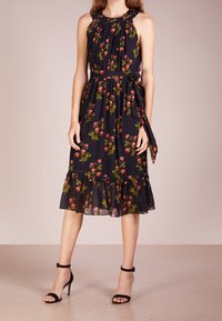 Schwarzes Blumenkleid mit Halterneck, Ausschnitt-Detail, leuchtend pinken Rosen und grünen Blättern, gerafftem Saum und passendem Taillengürtel.