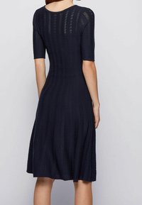 Marinblå ribbstickad klänning med korta ärmar, figurnära bodice, utsvängd kjol och öppet arbetade detaljer vid axlarna och midjan.