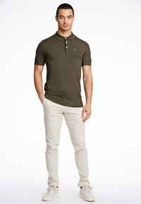 Mörkgrön kortärmad polo med ribbad textur, treknappsslå och diskret logotypdetalj, ihop med ljusbeiga slim-fit byxor.