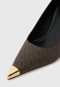 Zapato de tacón alto con estampado marrón, punta afilada y capucha metálica dorada en la punta, con un forro interior negro y liso.