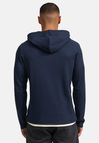 Hoodie in Marineblau aus strukturiertem, geripptem Stoff; mit einer großen Kapuze und langen Ärmeln, die bis zur Hüfte reichen und einen leicht abgerundeten Saum haben.