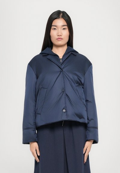 Mørkeblå pufferjakke med en cropped design, knaplukning, stort krave og sidelommer, der har en glat, blank overflade.