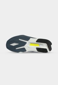 Εξωτερική σόλα αθλητικού παπουτσιού New Balance με μαύρα και σκούρα μπλε σχέδια στη σόλα και κίτρινη ετικέτα "new balance" στη μέση σόλα.