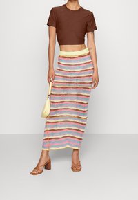 Brun kortärmad t-shirt med ribbad textur. Flerfärgad stickad maxikjol med horisontella randningar och gul midja. Bruna klacksandaler med blockklack.