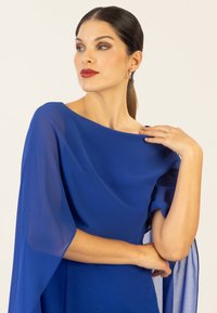 Blaues Kleid mit einem weiten, drapierten Ausschnitt und fließenden, durchsichtigen Ärmeln. Glatter Stoff mit leichter Struktur, der eine moderne Silhouette betont.