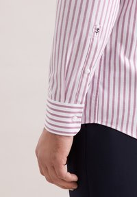 Camicia a maniche lunghe con sottili strisce rosse e bianche, con polsini abbottonati e un logo del marchio ben visibile ricamato sulla manica.