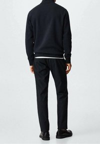 Felpa scura con collo alto, abbinata a pantaloni neri slim fit e scarpe nere. Presenta materiale strutturato e polsini a coste.