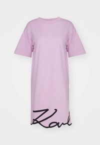 Fioletowa, oversize sukienka koszulowa z bawełny, z krótkimi rękawami i czarnym, sygnaturowym nadrukiem na dole. Gładka faktura, luźny krój.