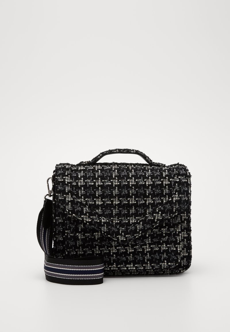 Sac à main texturé noir et blanc avec poignée supérieure et bandoulière noire amovible avec des rayures blanches et grises, posé à plat devant.