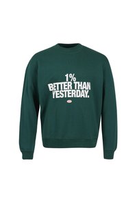 Grønn hettegenser med ribbet tekstur, rund hals og lange ermer. Har stor hvit tekst: "1% BEDRE ENN I GÅR" på forsiden.